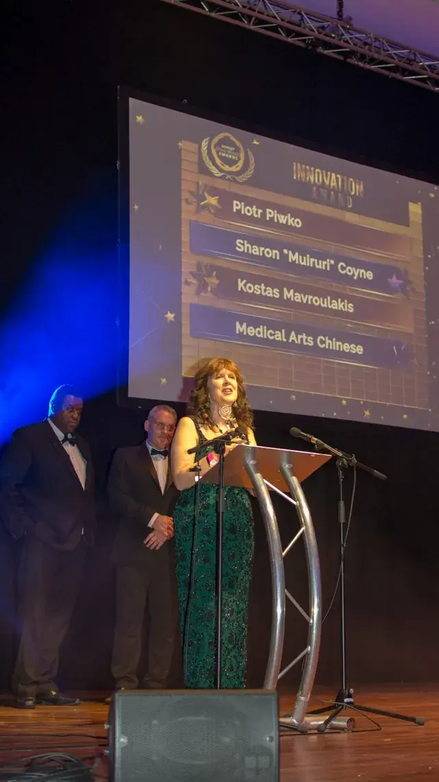 The host addressing guests from the lectern as finalists appear on the big screen